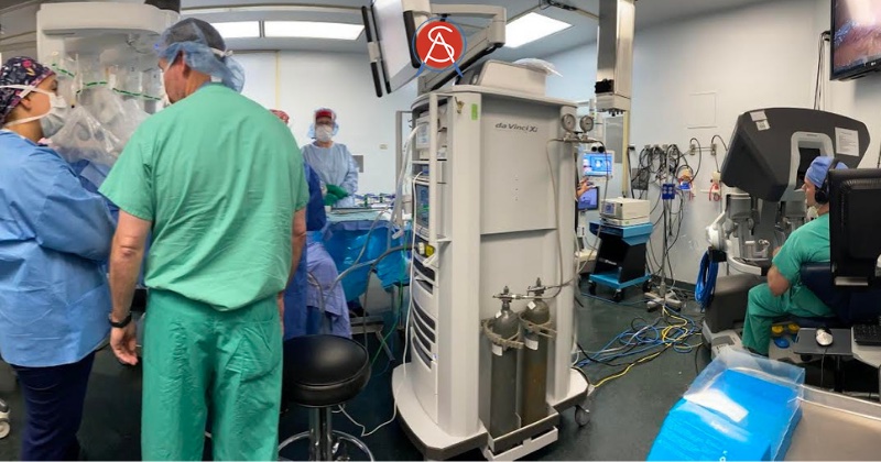 Dr. Forrest Ringold’s operating team prepares to bring a live broadcasted robotically assisted gastric bypass surgery during Intuitive’s Connect Up Robotics Forum 2021. The Da Vinci robotic surgical system sits at center with surgeon at console to right and OR staff with patient at left under surgical robotic arms.