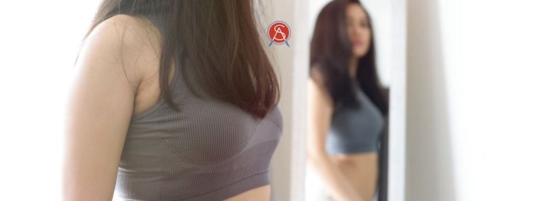 Woman looks in mirror thanking her body for all it does for her and is capable of to improve her body image as recommended by the team at Surgical Association of Mobile 