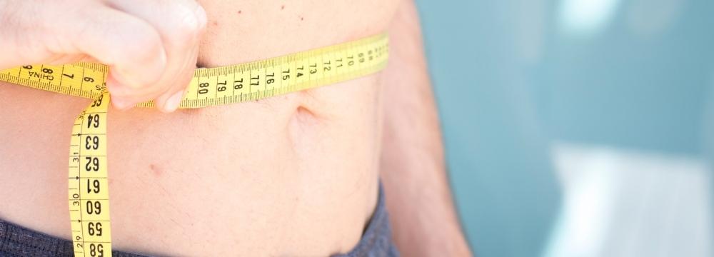 Man measuring stomach size with measuring tape to qualify for obesity under new bariatric surgery guidelines