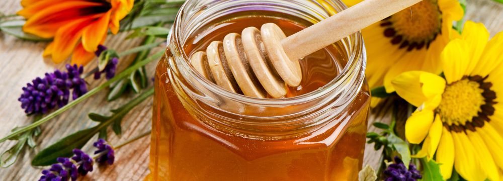 Honey jar with honey comb sticking out surrounded by flowers