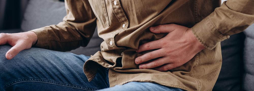 Man hunched over on couch grabbing stomach due to intense pain 